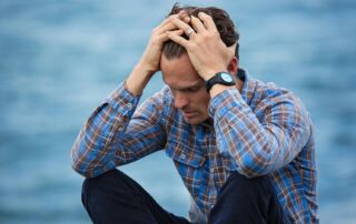man with ptsd sitting on ground in front of the water